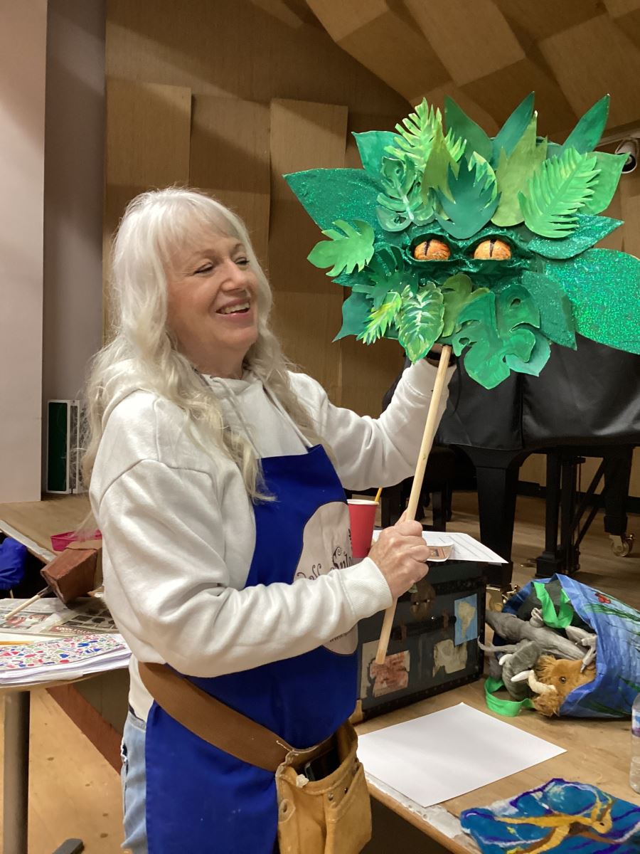 The artist holding up her puppet that looks like a bush with yellow eyes poking out