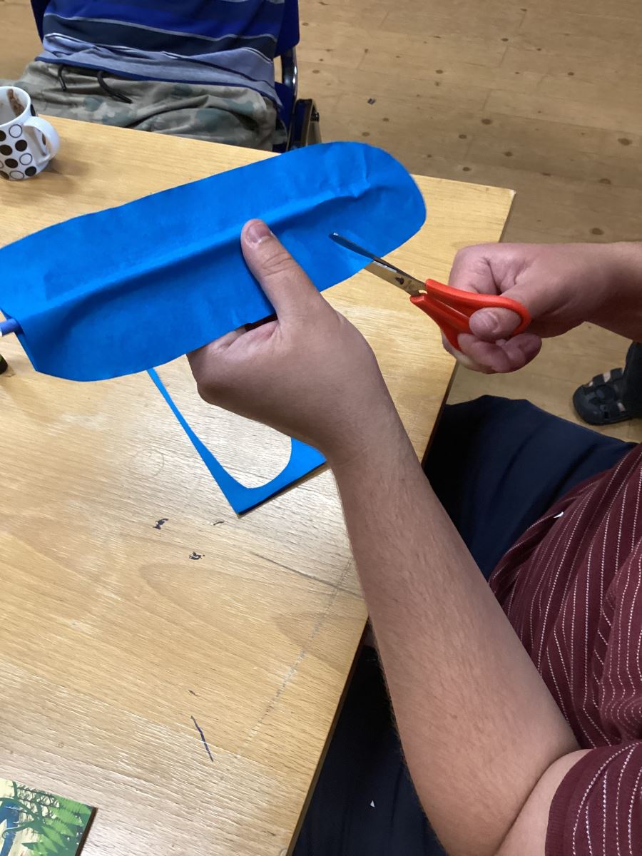 A person cutting a blue paper feather