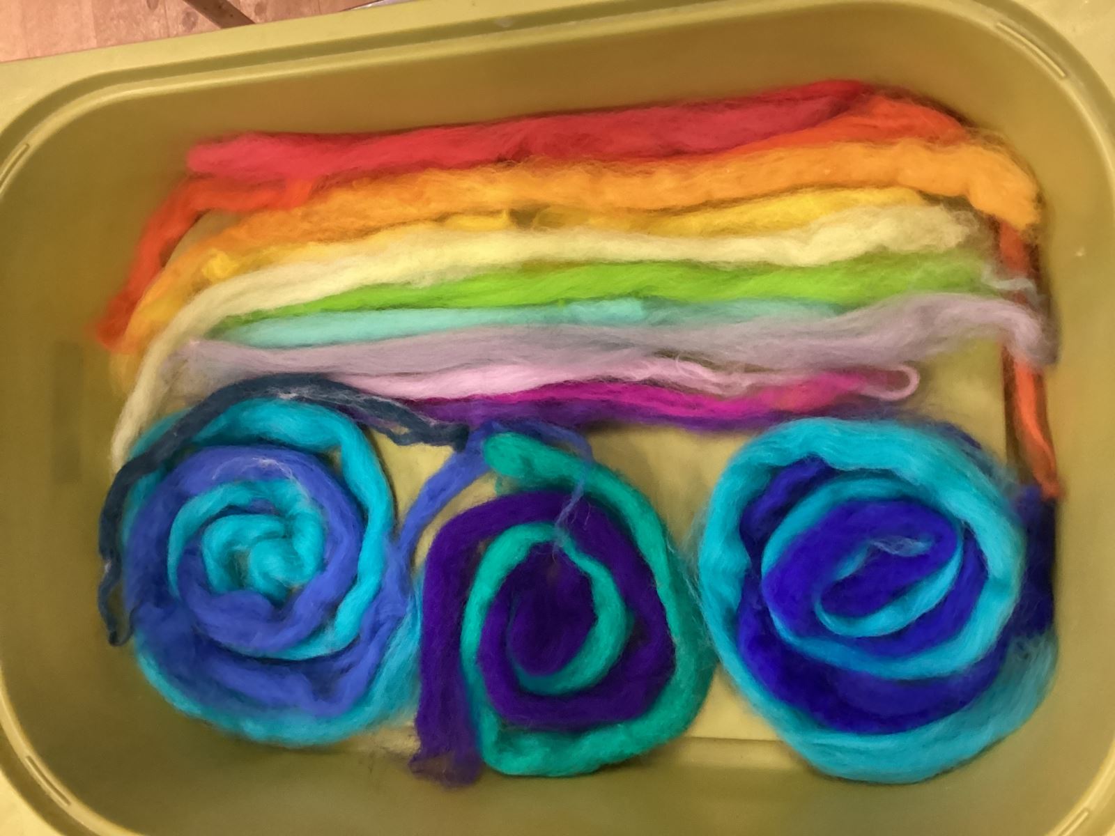 Felt in a tub that looks like a rainbow on the left and blue and purple swirls on the right