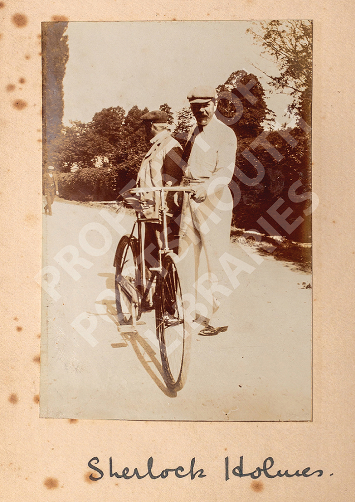 a Photograph of Conan Doyle standing with another man and a bicycle with the caption of Sherlock Holmes in Conan Doyle's handwriting